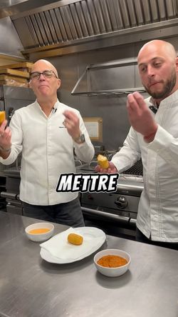 Deux chefs dans une cuisine de restaurant dégustent des bouchées avec des sauces sur une table en inox.