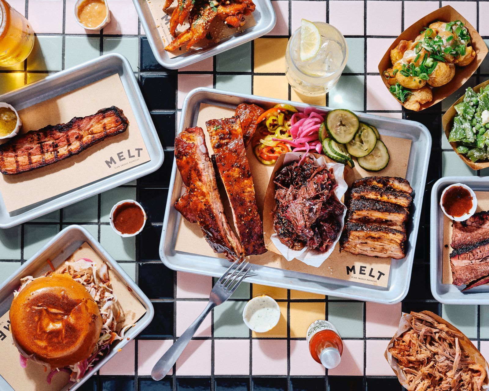 Barbecue Texan and pulled pork dishes served with pickles and sauces on metal trays at MELT Pantheon.
