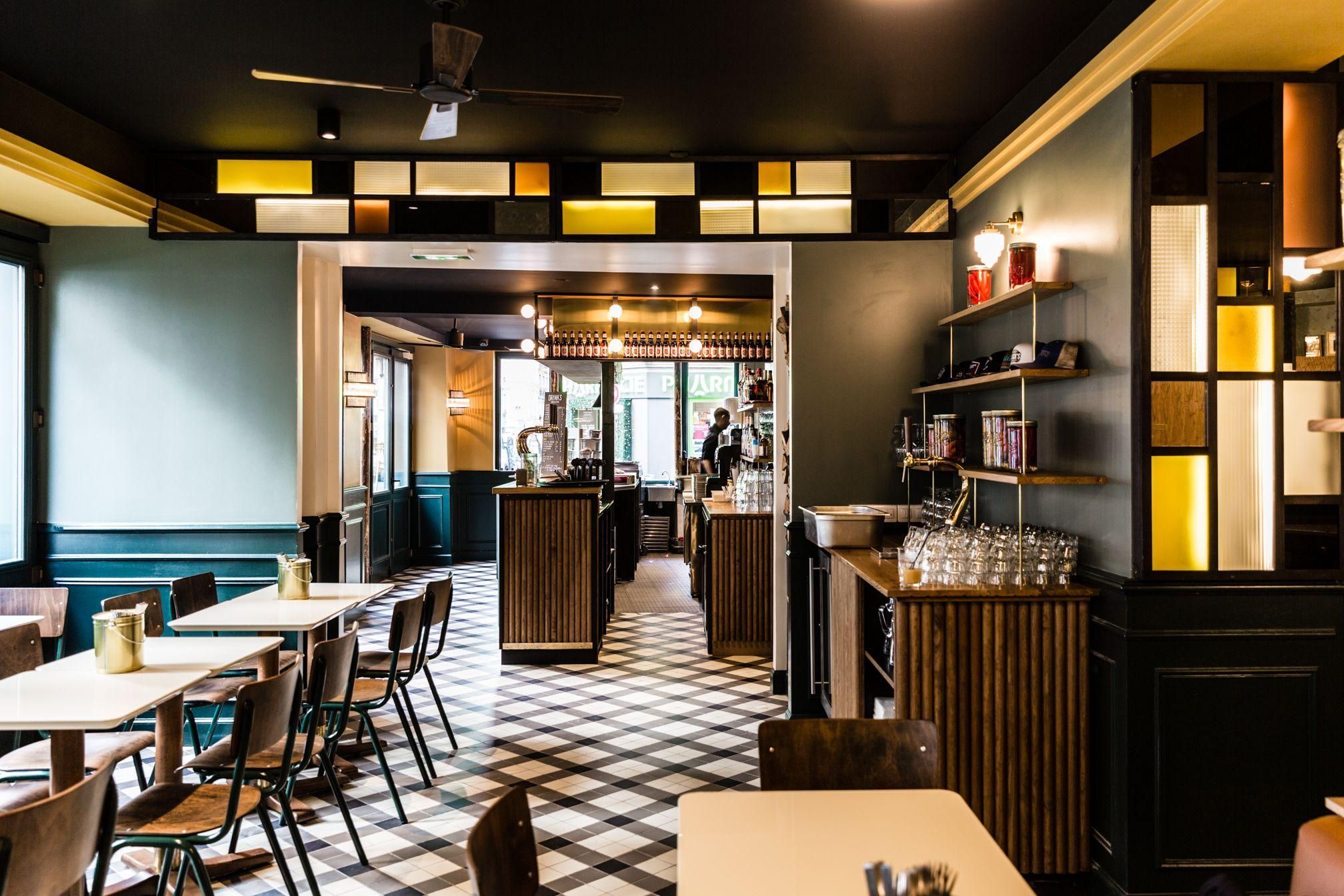 Intérieur moderne et lumineux de MELT BATIGNOLLES avec tables en bois, chaises métalliques et sol en damier noir et blanc.