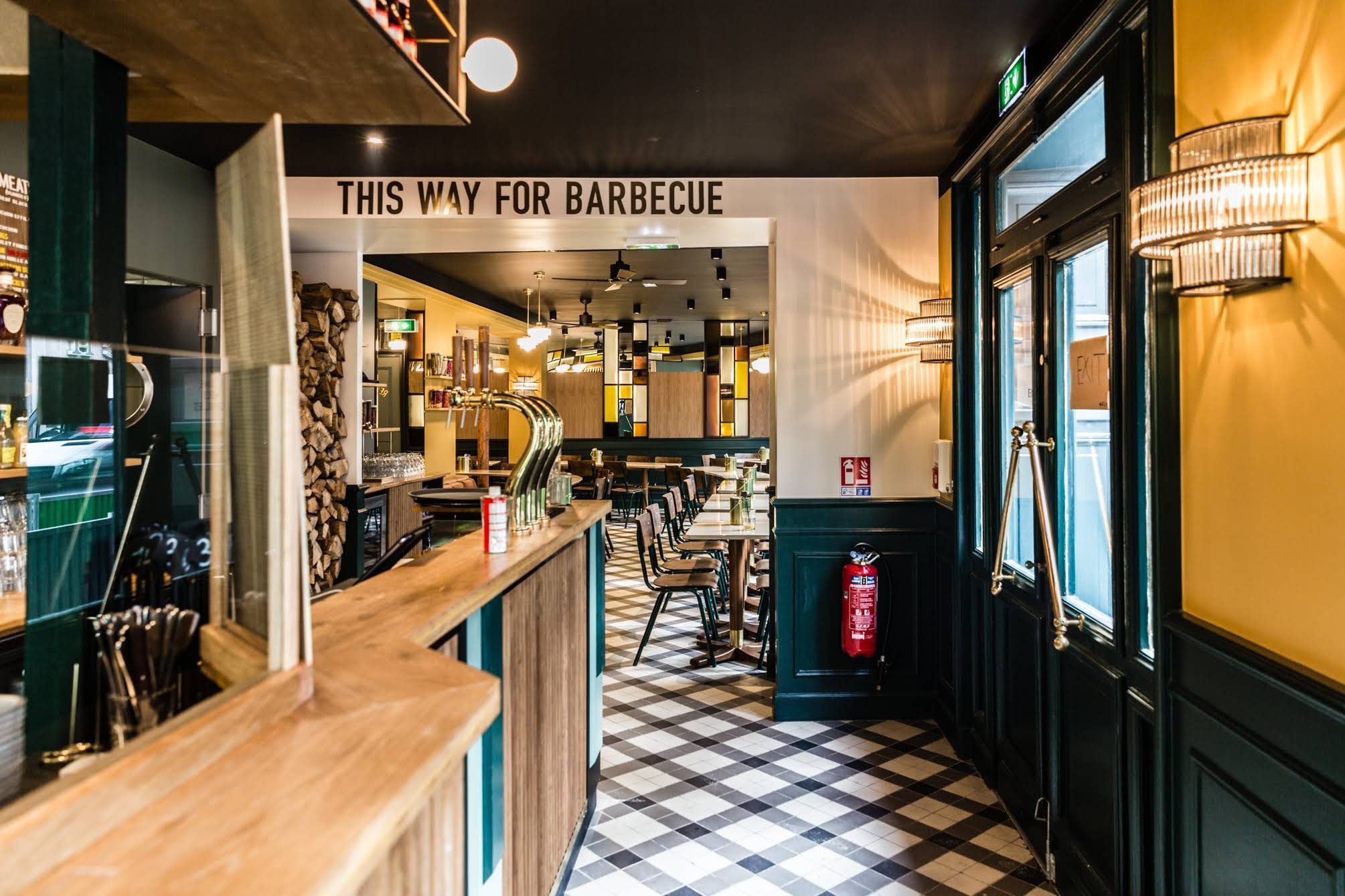 Intérieur de MELT BATIGNOLLES avec un comptoir en bois, sols à carreaux et panneau indiquant barbecue texan.