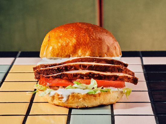 A savory sandwich featuring layers of brisket, lettuce, and tomato, served on a golden bun.