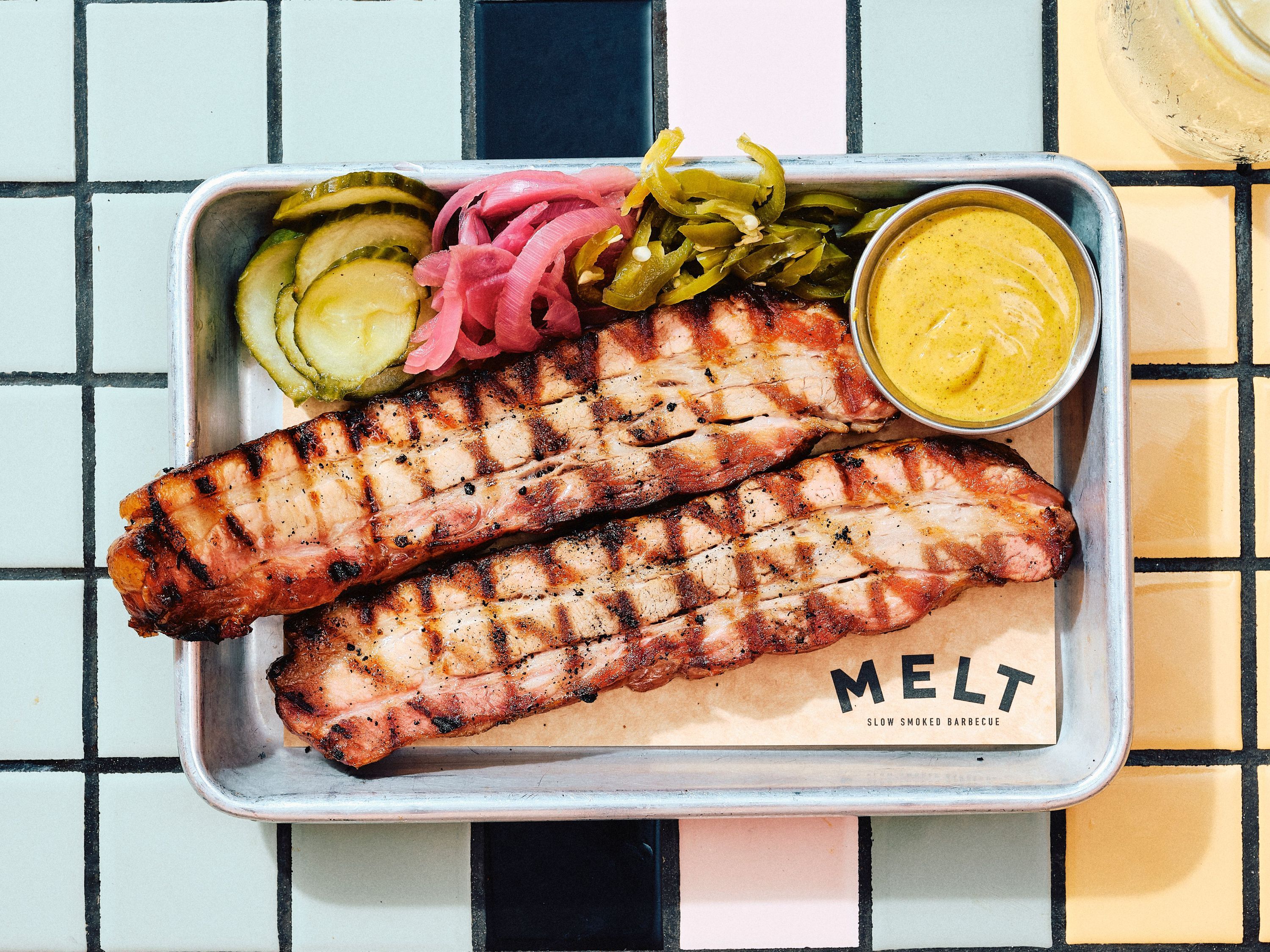 Planches de côtes barbecue accompagnées de cornichons, oignons, piments et de sauce moutarde.