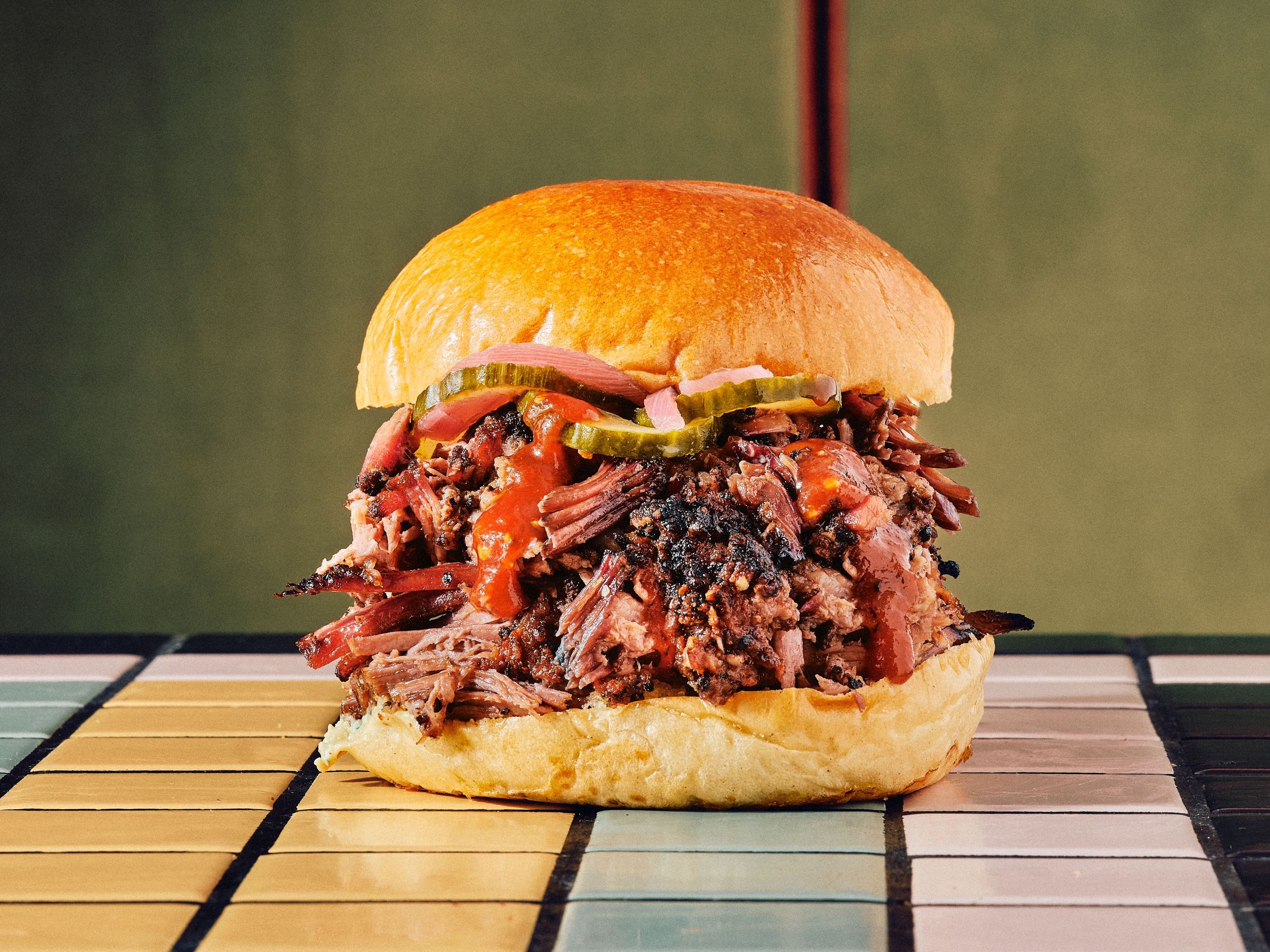 Savoureux sandwich avec pulled pork, garnitures de sauce, oignons et cornichons, servi dans un pain moelleux.