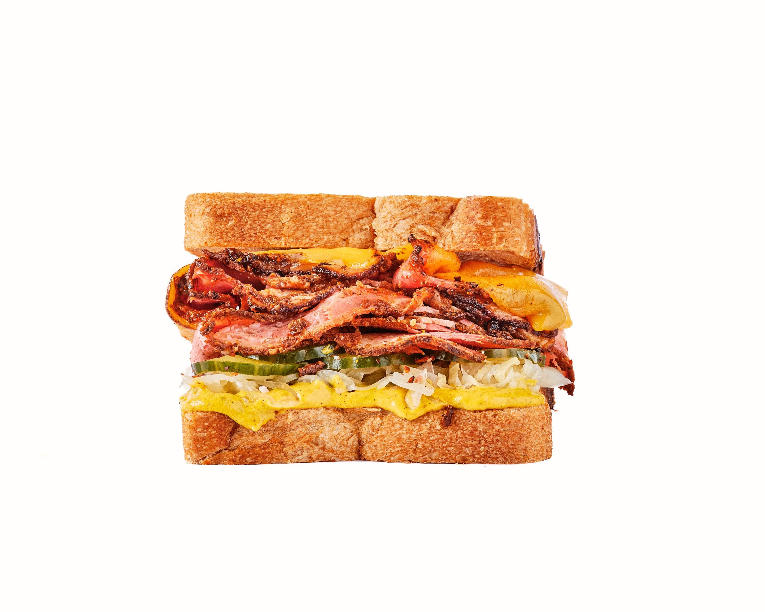 Sandwich au brisket, bacon croustillant, légumes variés, et sauces, servi dans du pain de mie.