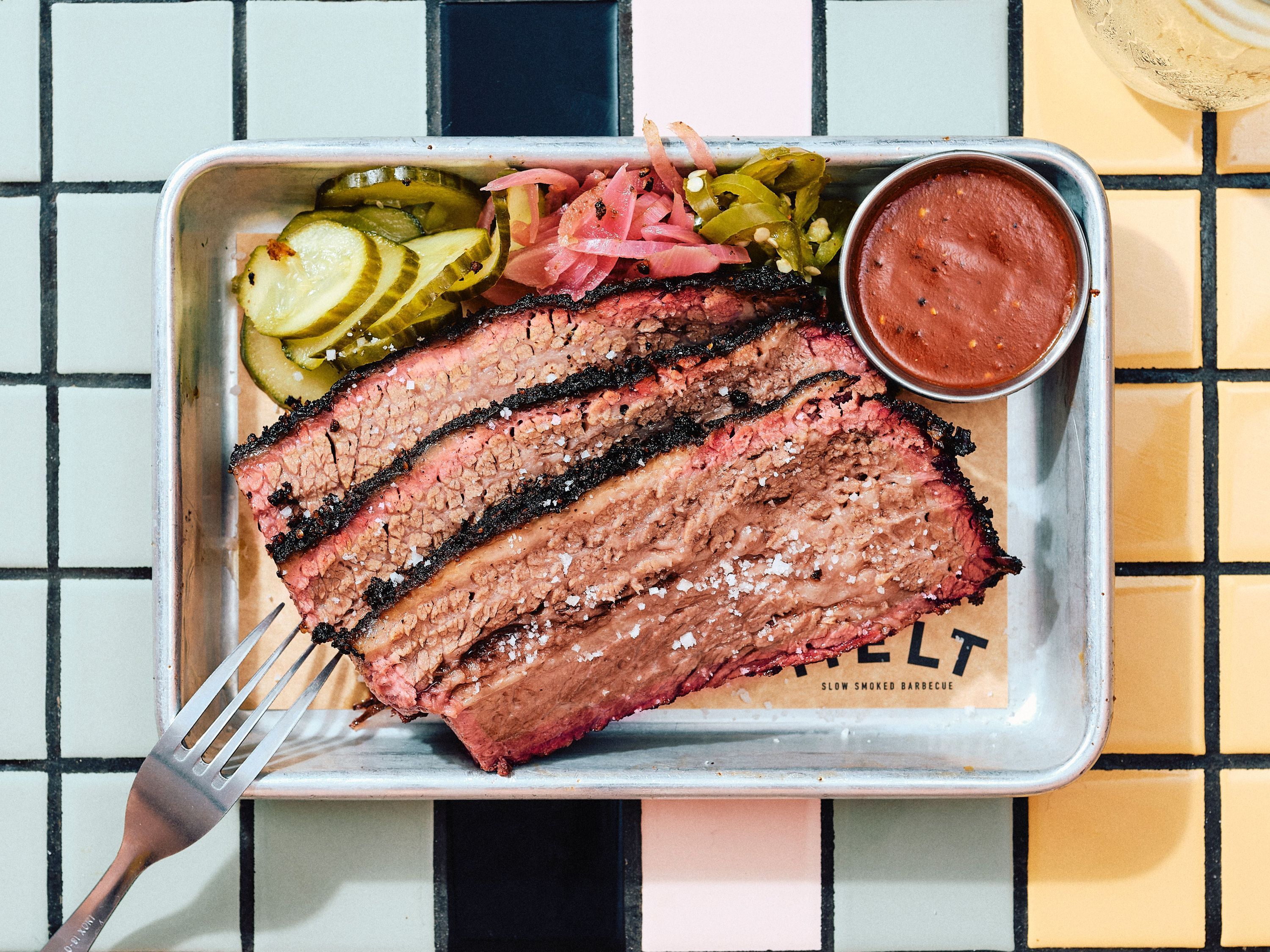 Sliced brisket served with pickles, onions, and barbecue sauce on a metal tray at MELT Pantheon.