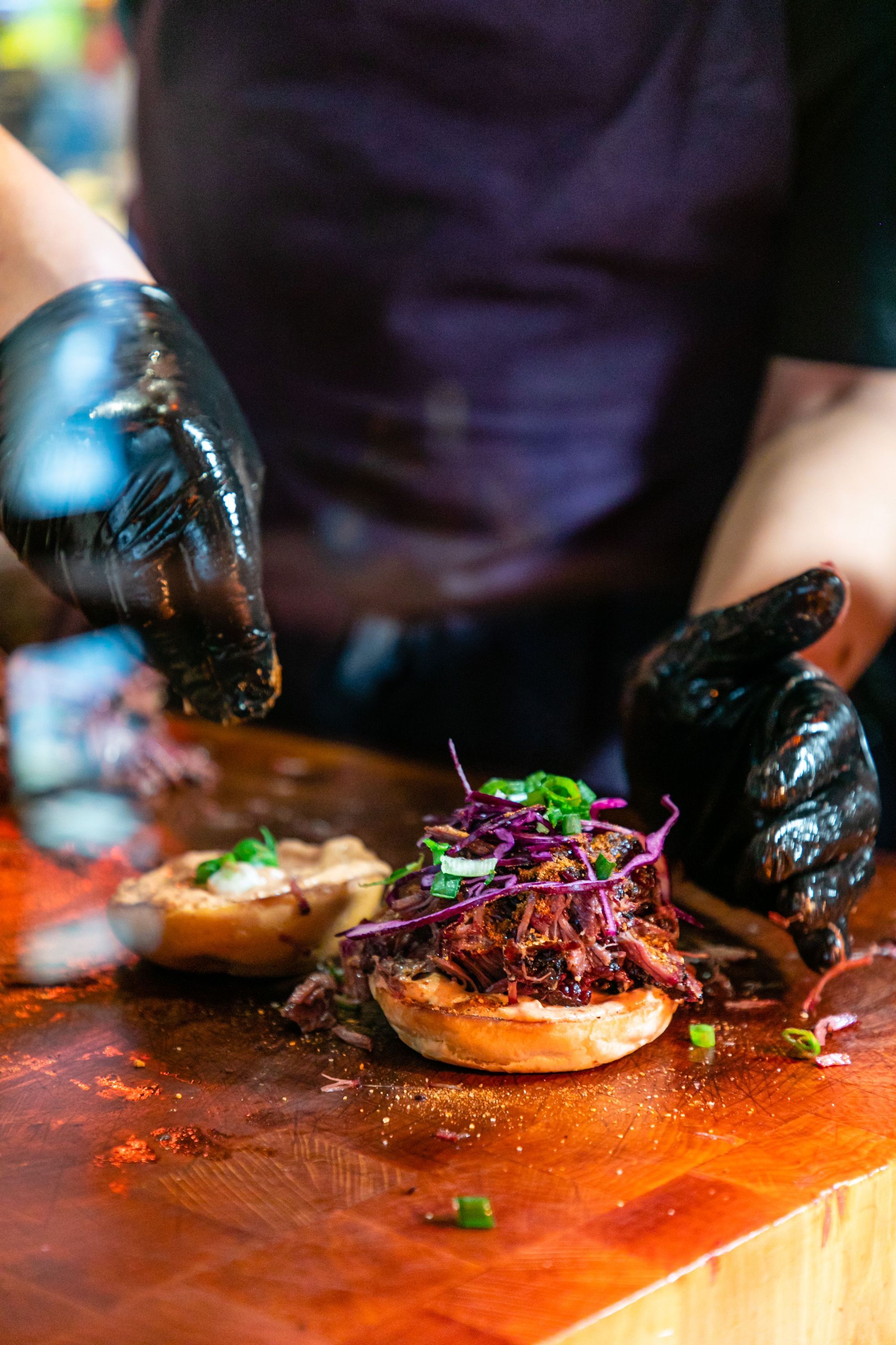 Préparation d'un sandwich avec du brisket et du pulled pork, sur une planche en bois.