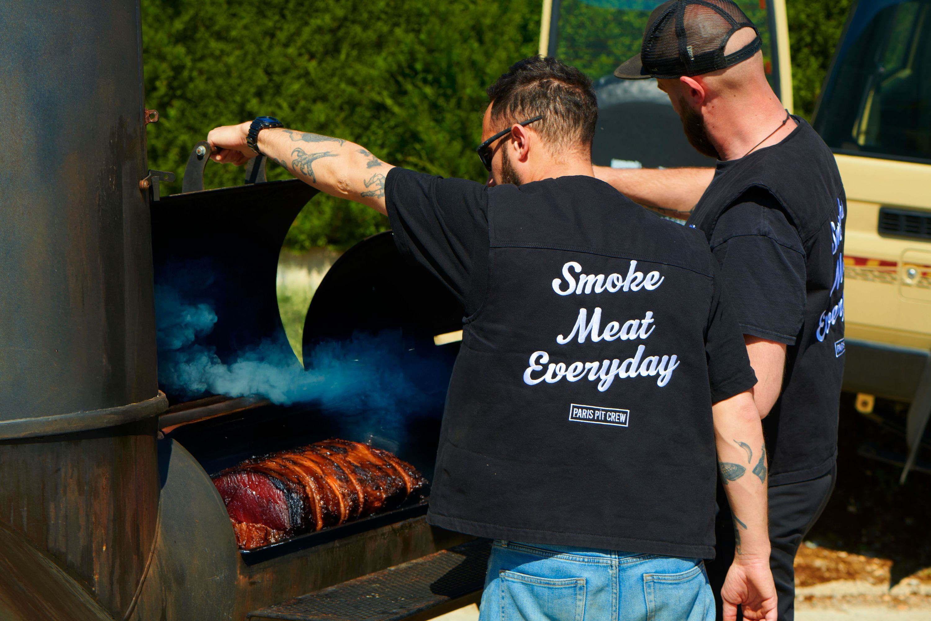 Two chefs preparing brisket on a barbecue grill, showcasing a smoke-filled atmosphere.