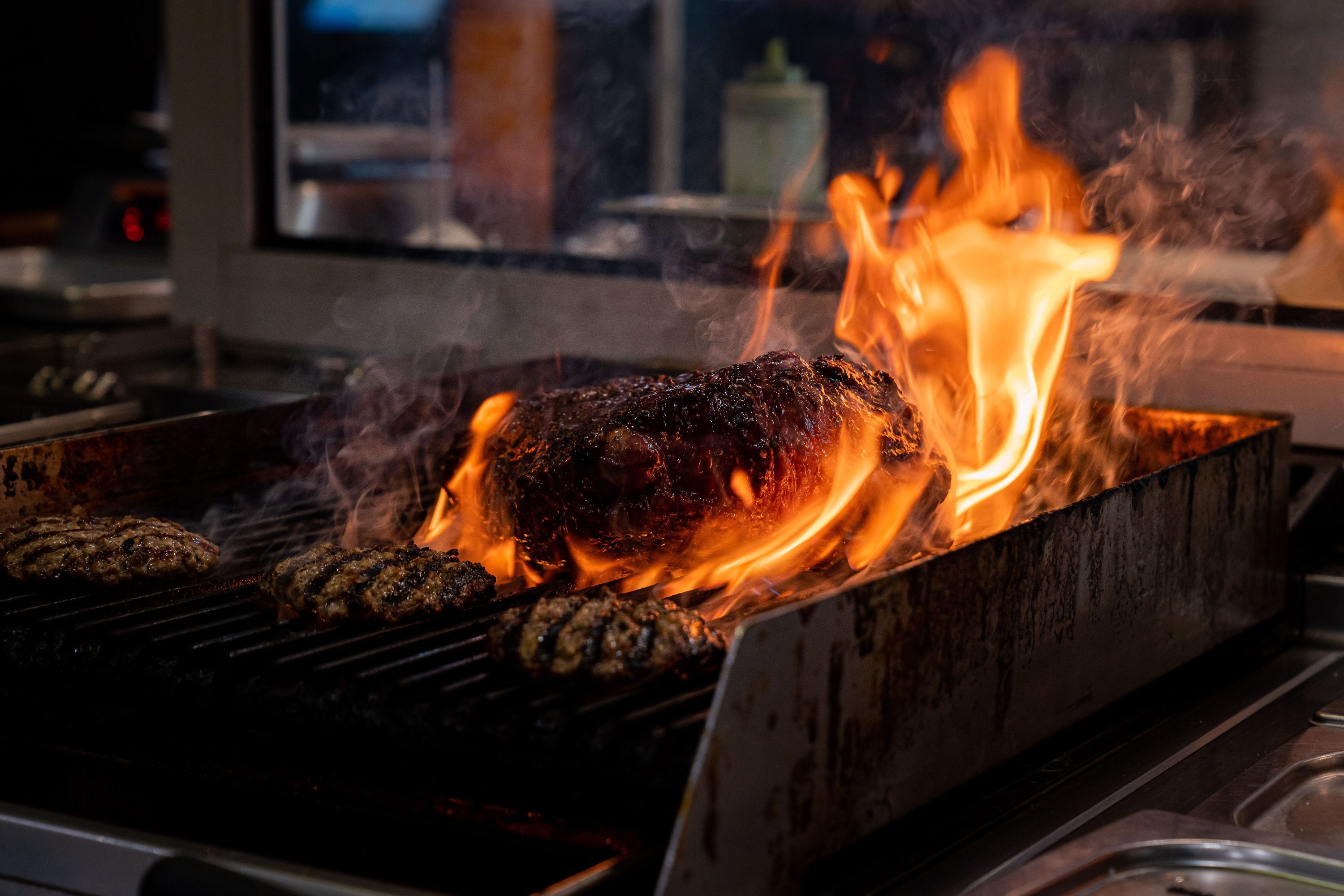 A barbecue grill featuring a flame-cooked brisket alongside sizzling patties.