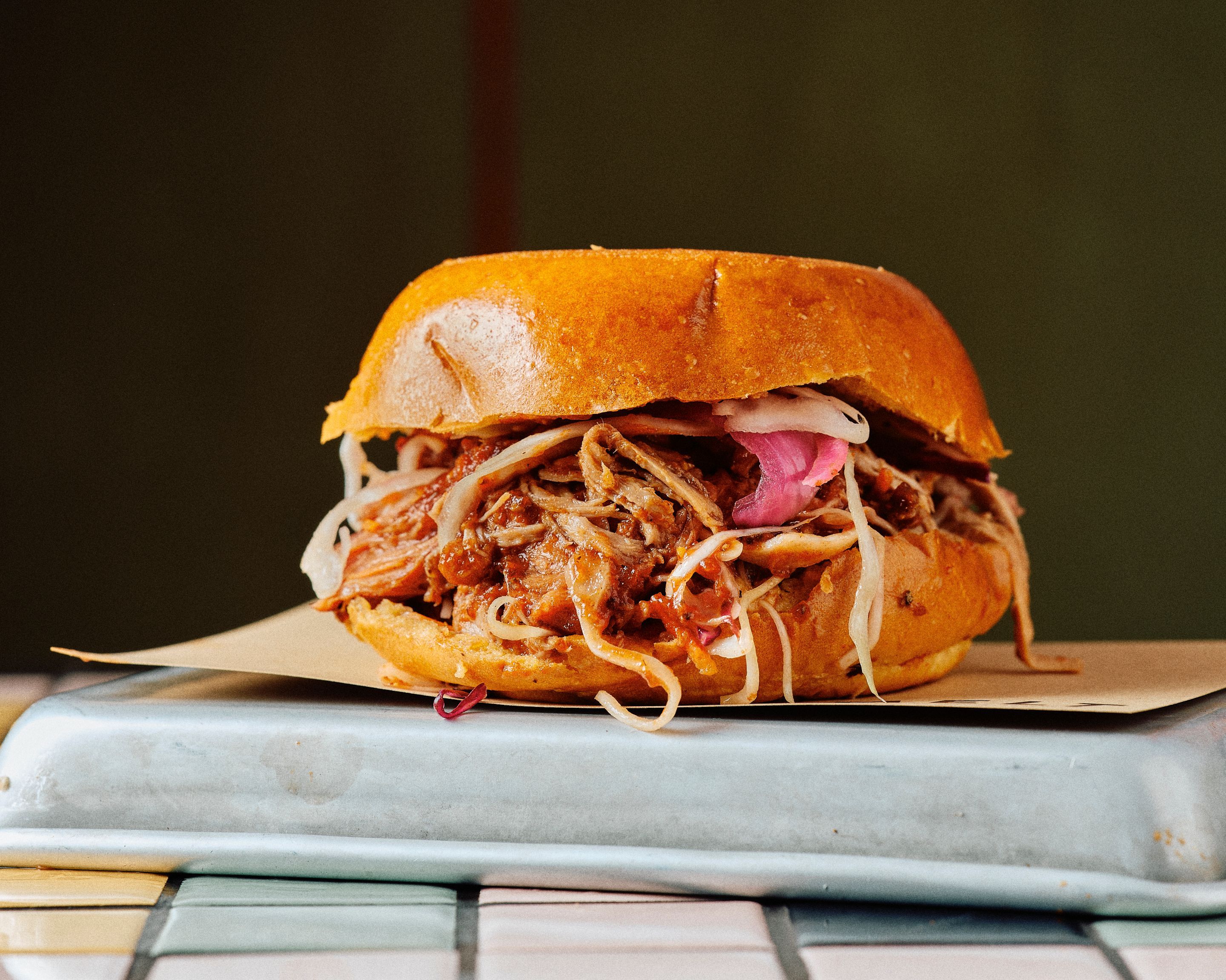 Sandwich au pulled pork sur pain, garni de chou et d'oignons, présenté sur une plaque.