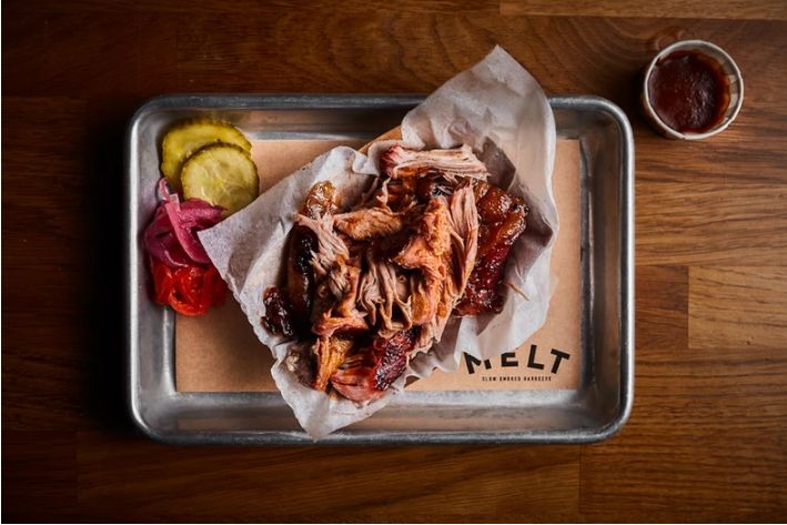 Tender pulled pork served on parchment paper with pickles, tomatoes, and onions at MELT BATIGNOLLES.
