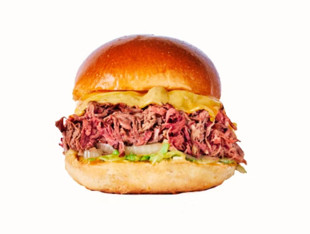 A close-up of a sandwich filled with tender brisket, lettuce, cheese, and a soft bun.