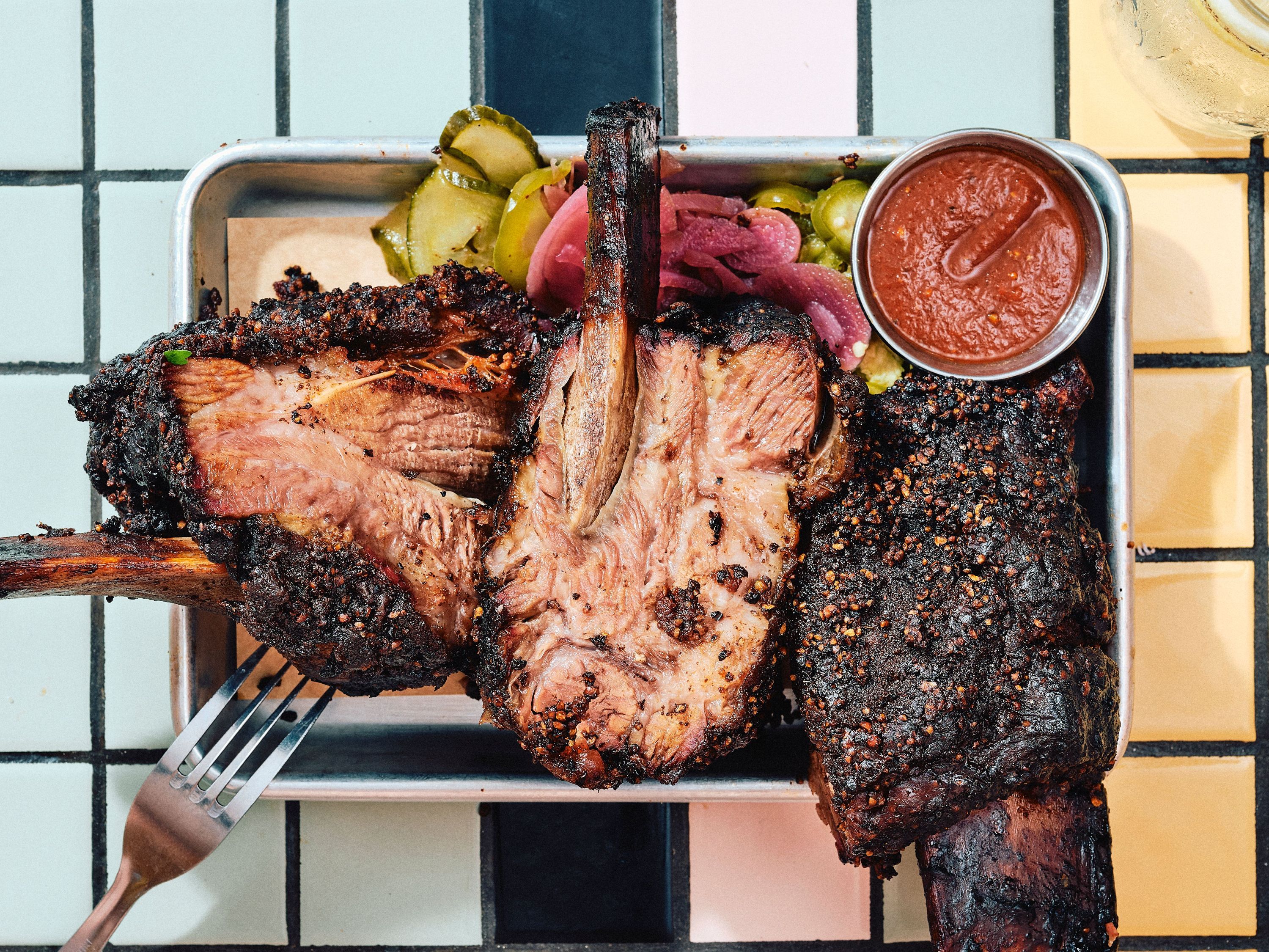 Tender smoked brisket served with pickles, onions, and barbecue sauce in a stainless steel tray.