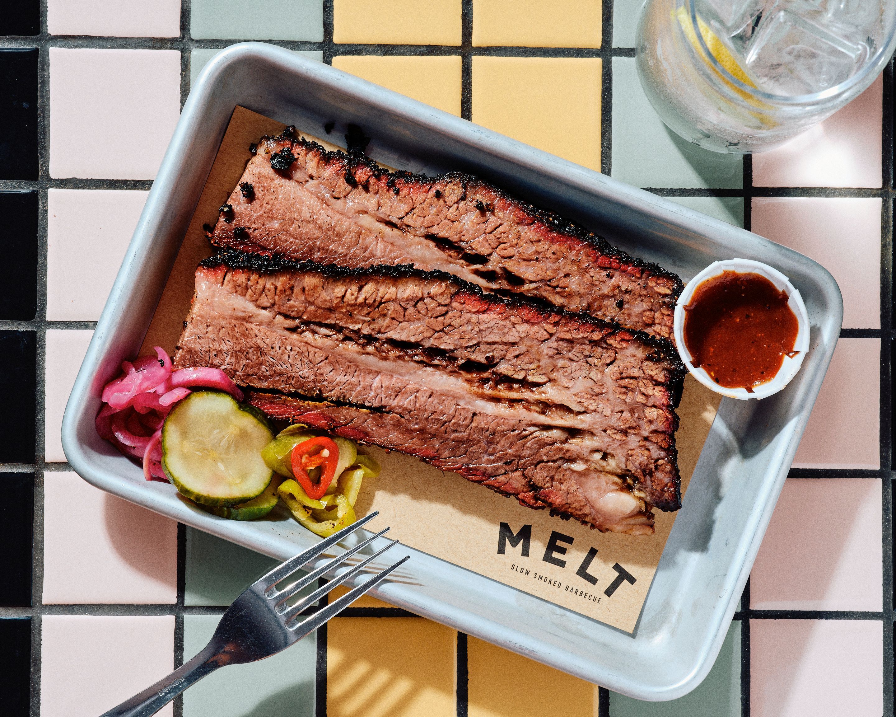 Tranches de brisket cuit, accompagnées de pickles et d'une sauce barbecue, servies au restaurant MELT.