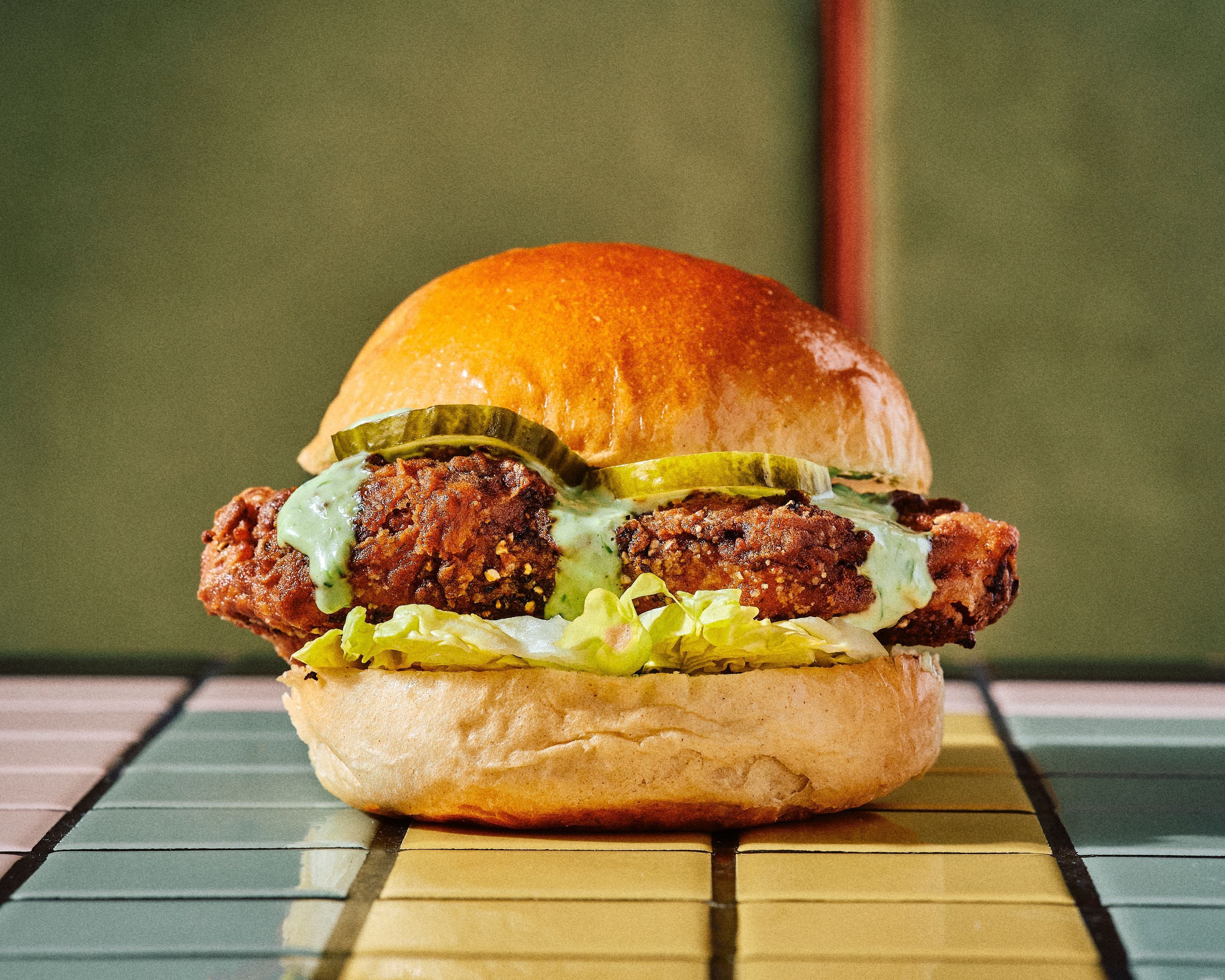Sandwich barbecue à la viande avec cornichons, laitue et sauce verte dans un pain brioché au restaurant Melt Oberkampf.