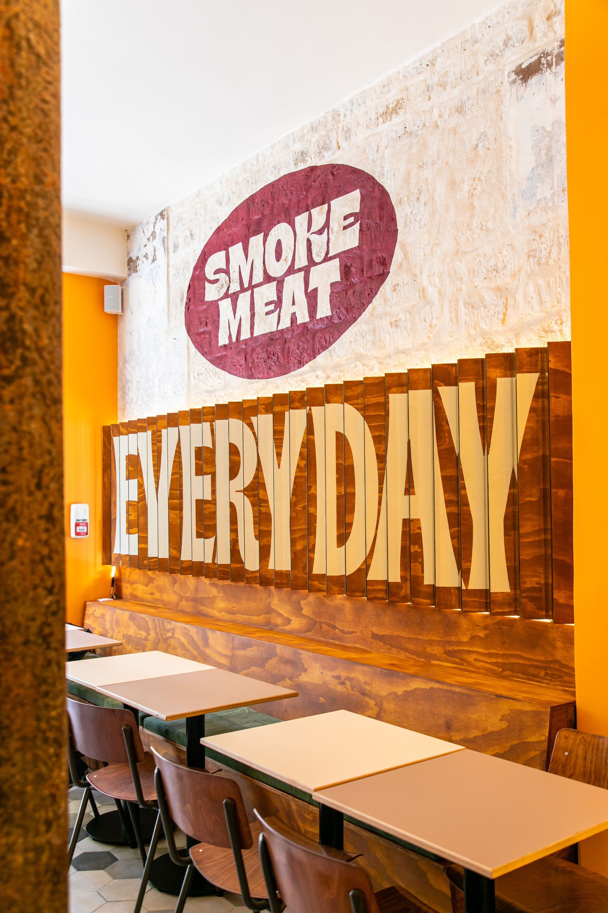 Intérieur du MELT DELI avec un mur décoré et des tables pour le barbecue texan et viande à Paris.