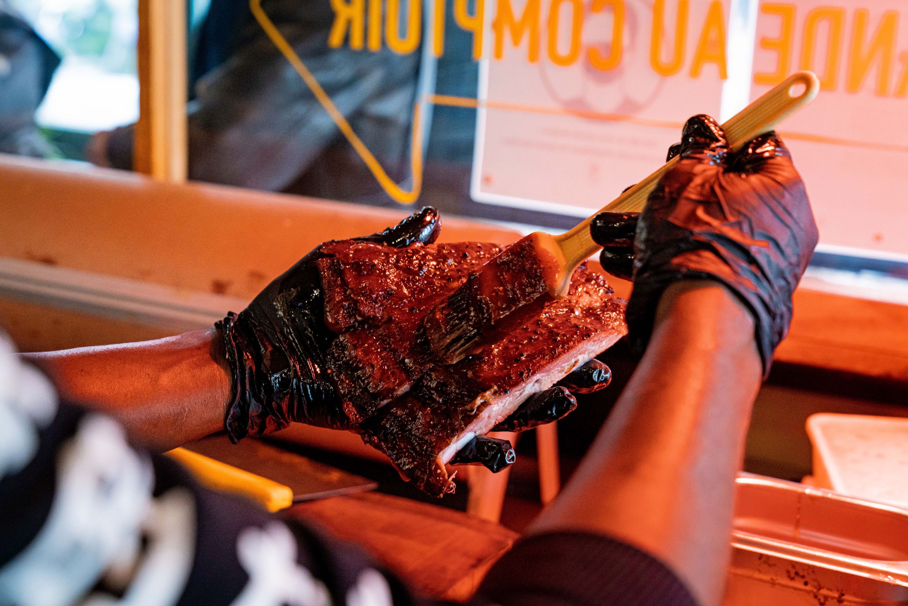 Des ribs de barbecue texan badigeonnés de sauce par un chef avec des gants noirs.