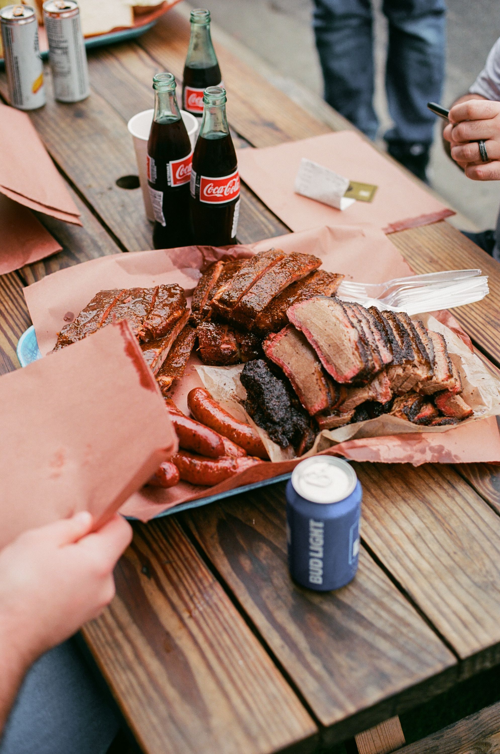A platter featuring brisket, pulled pork, and sausages, accompanied by soft drinks.