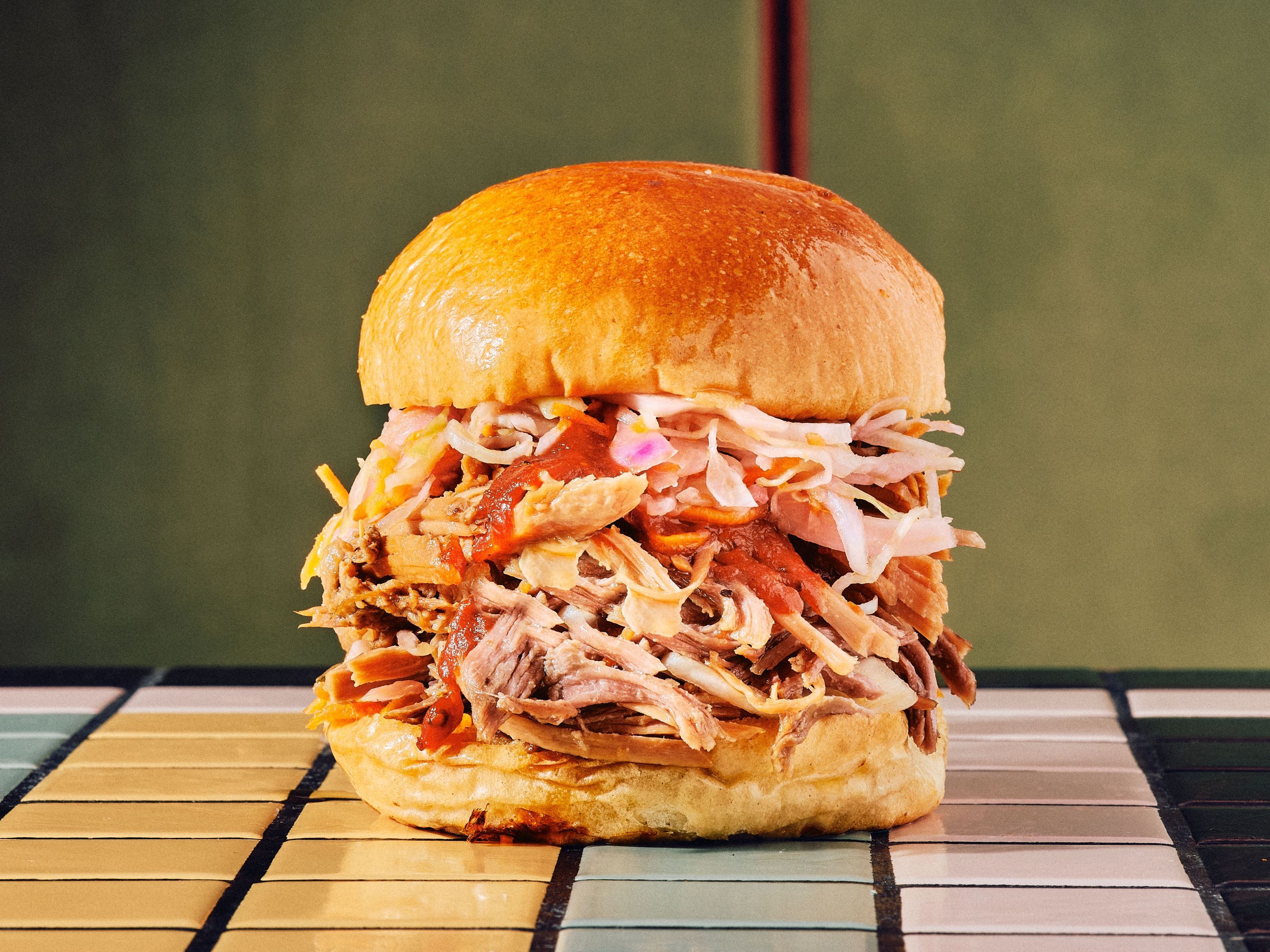 Sandwich garni de pulled pork, vinaigrette, et salade, servi dans un pain moelleux.