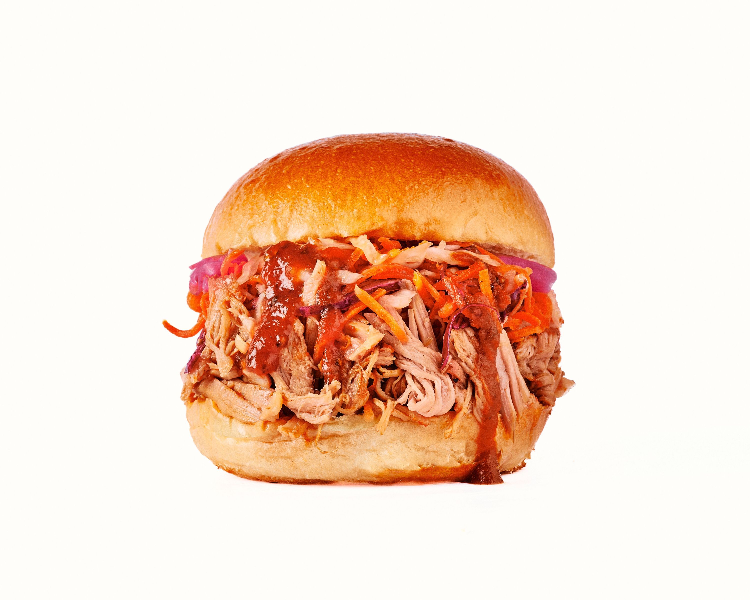 Sandwich avec pulled pork, sauce barbecue, et garnitures, servi dans un pain moelleux.